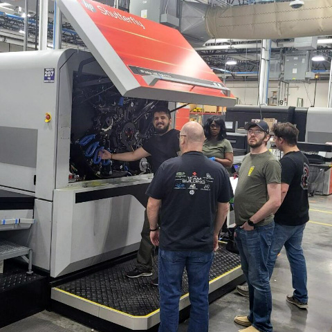 Shutterfly male apprentice working on a machine with three other people looking on 